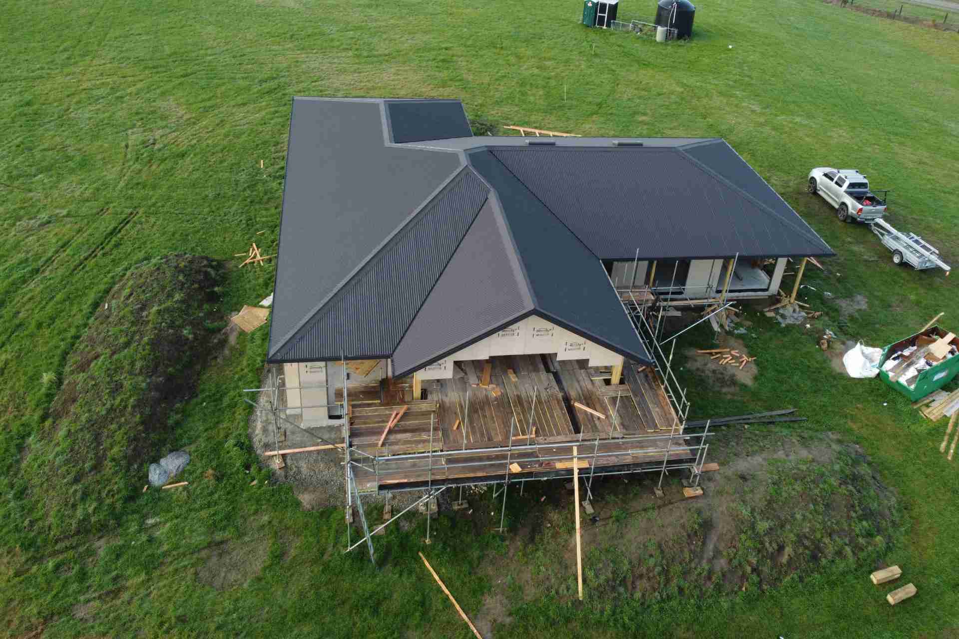 Aerial view of a house under construction with a dark metal roof and scaffolding around the deck
