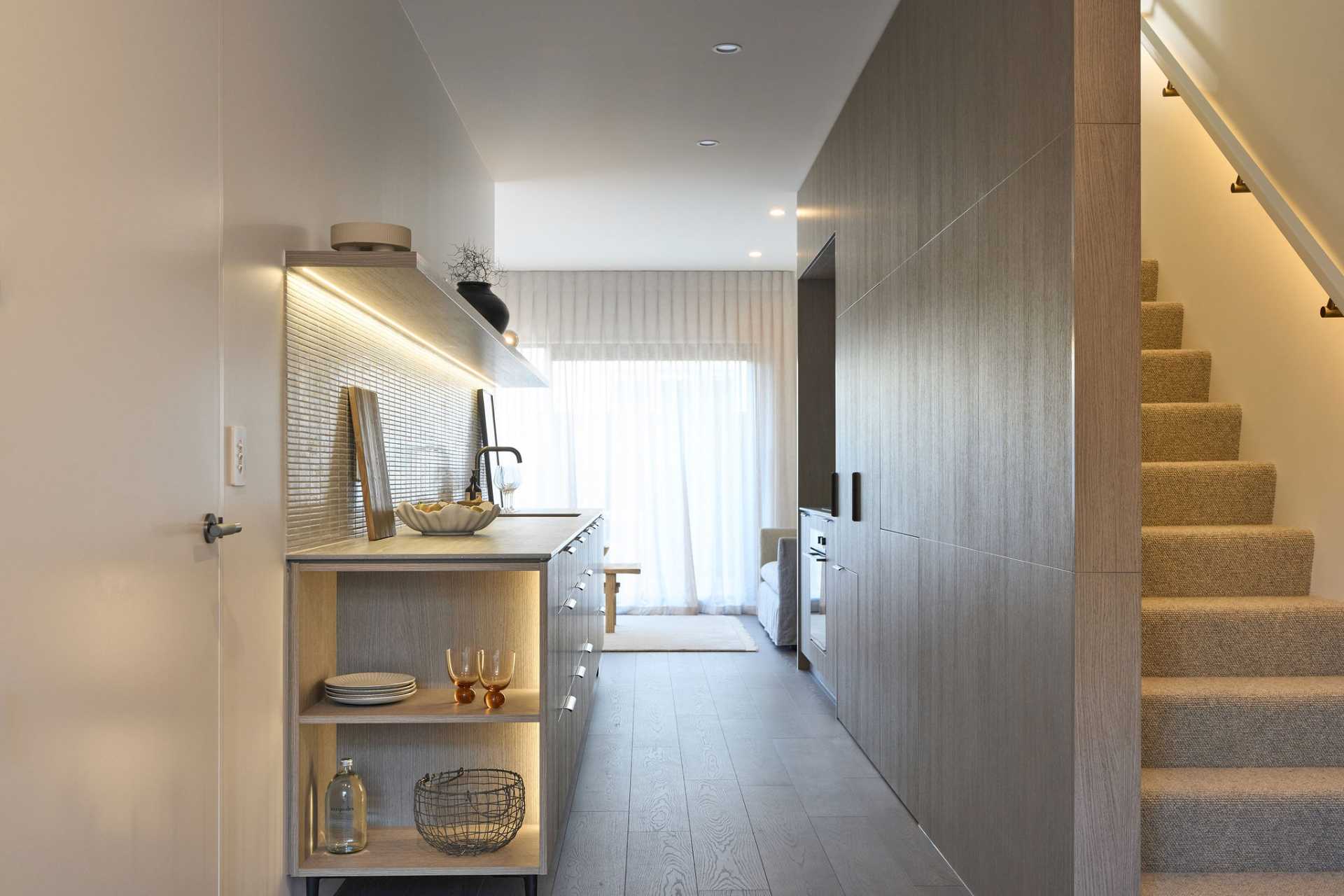 A bright kitchen with wooden cabinets, open shelves, and a staircase beside it.