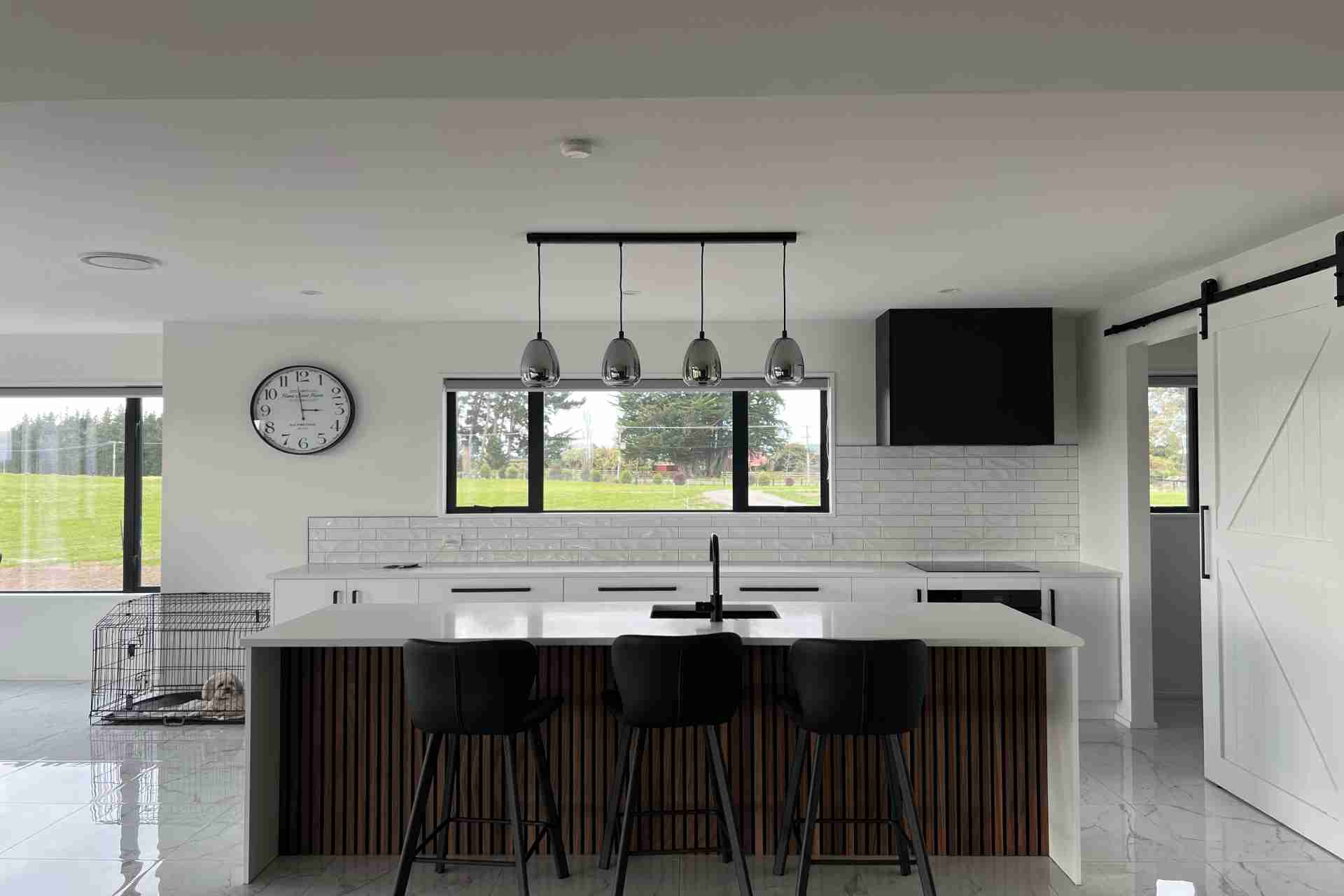 Sleek kitchen featuring a white island, black sink and fixtures, pendant lighting, sliding barn door, and window views of a rural landscape