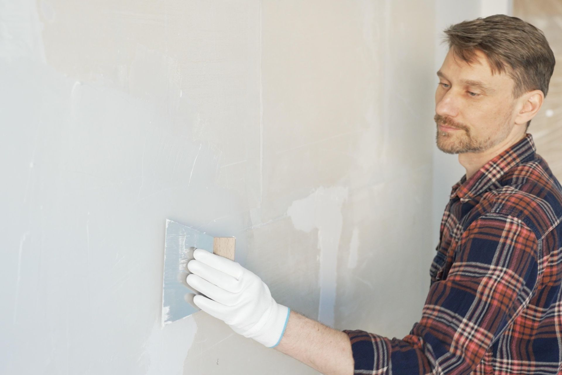 A close-up of a metal trowel smoothing fresh plaster on a wall surface.
