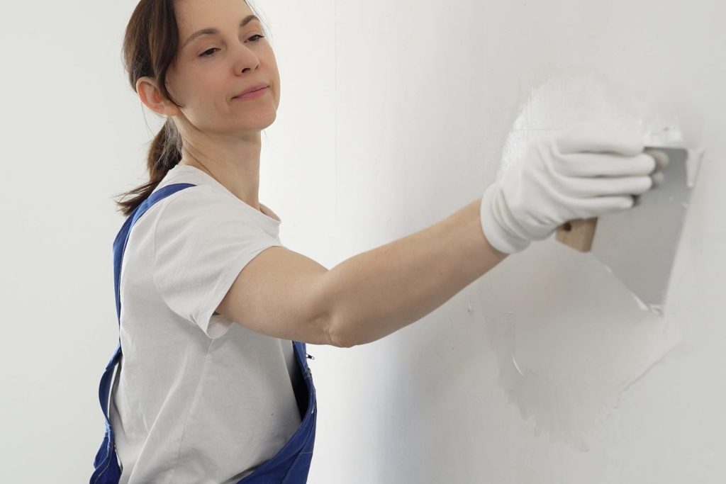 Someone spreading a thick layer of grey mortar onto a brick wall with a hand tool.