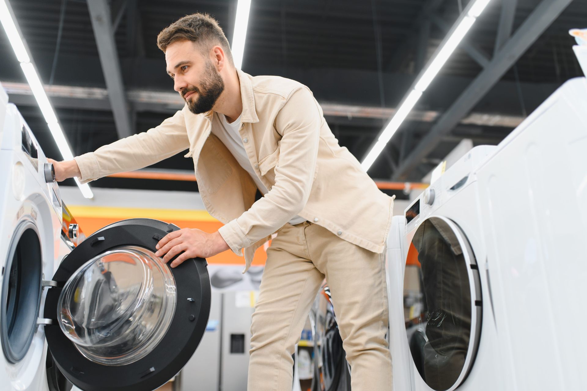 A man examining a front-loading washing machine in an appliance store.