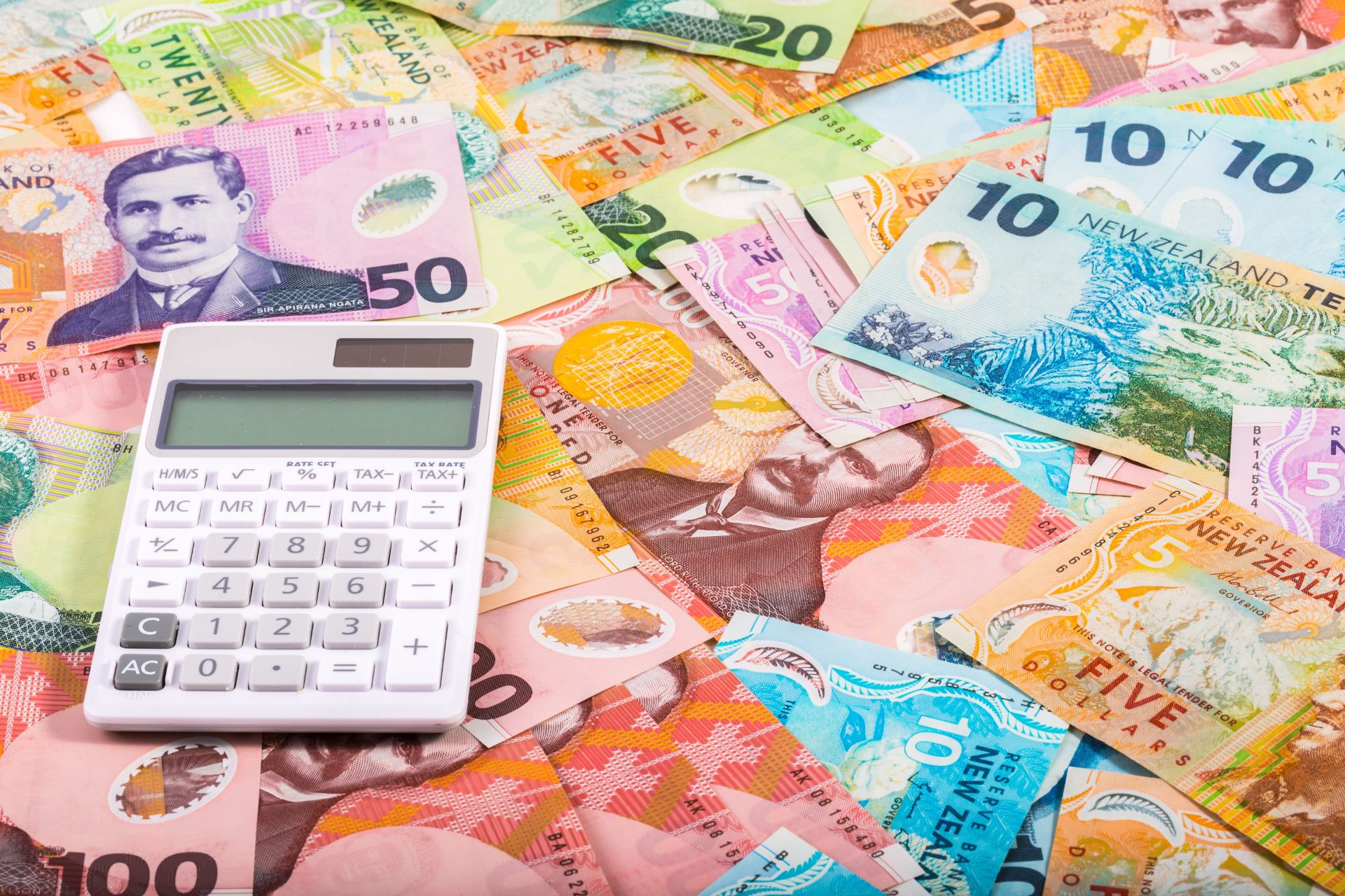White calculator resting on New Zealand banknotes.
