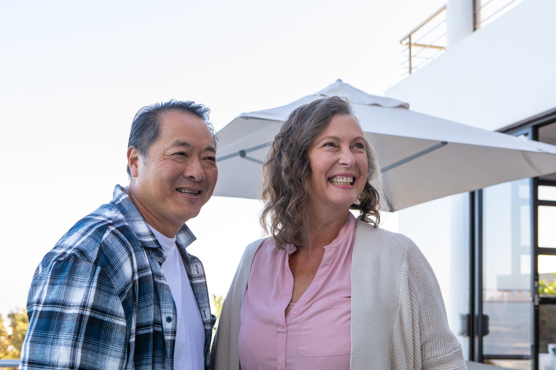 Middle-aged couple smiling outside a modern home, enjoying a relaxed lifestyle setting