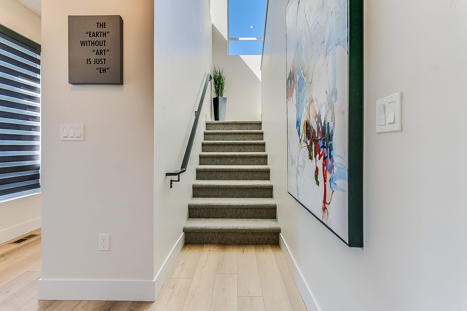 Bright modern hallway with carpeted stairs, wall art, timber flooring and natural light