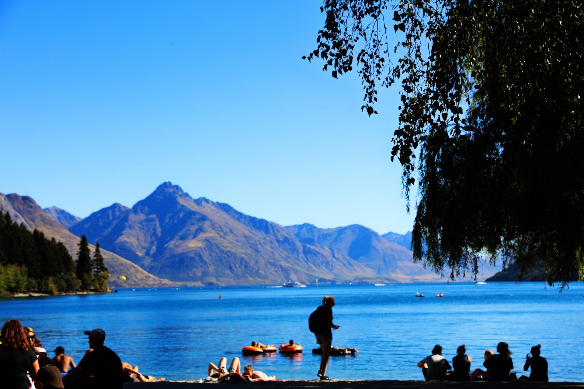 People relaxing beside a bright blue lake with mountains in the background