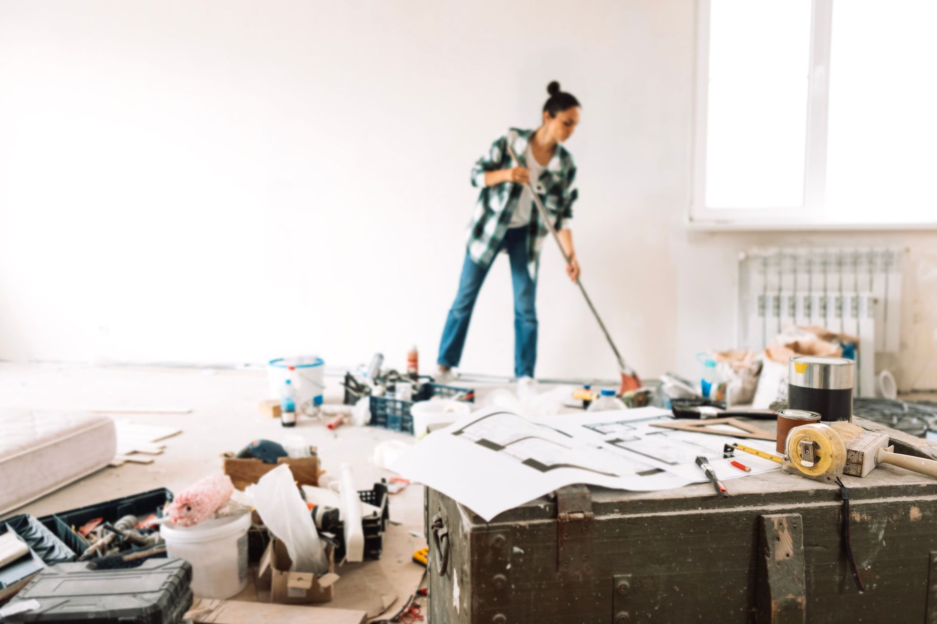 Homeowner sweeping during a messy home renovation with tools and plans in the foreground