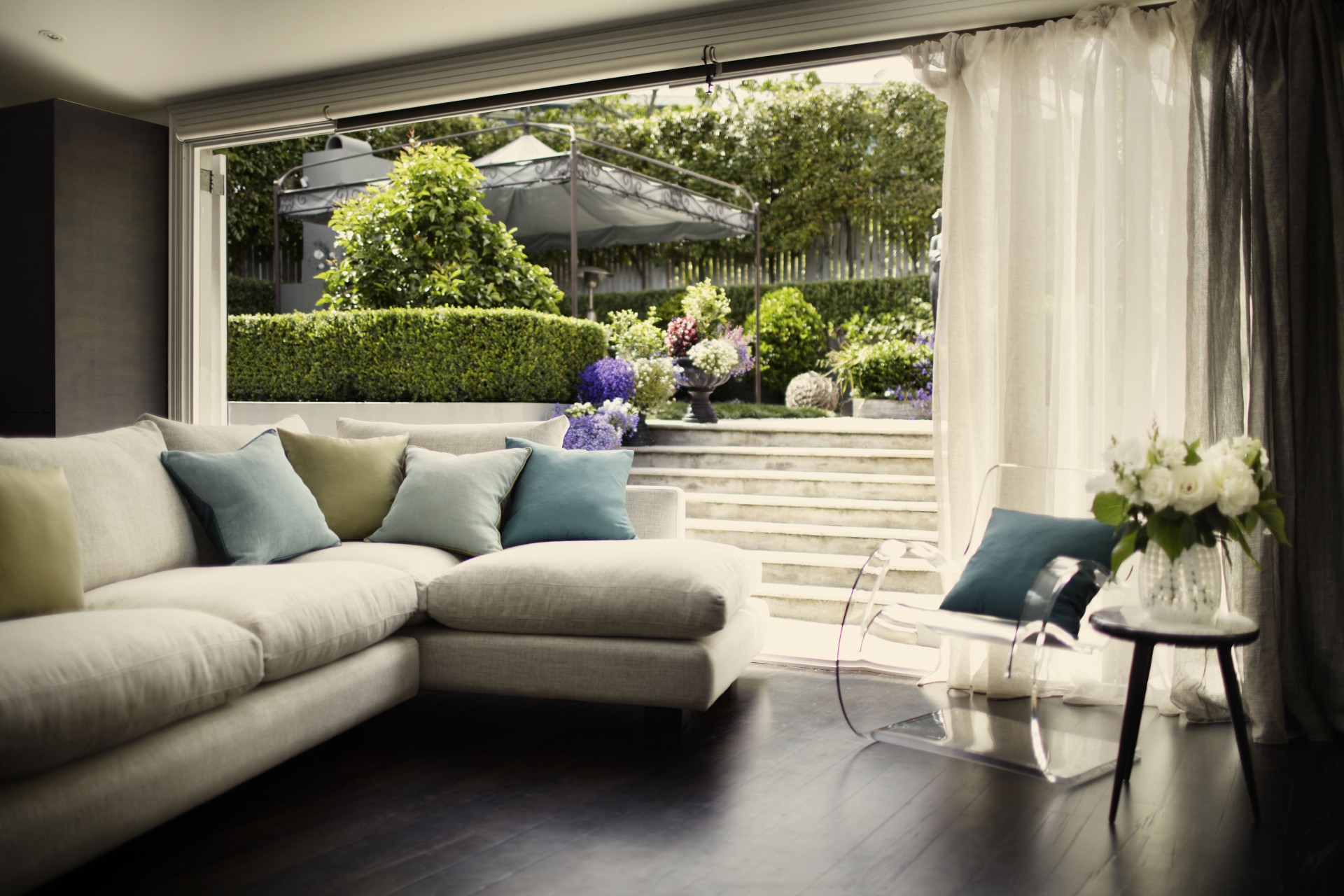 A bright living room with sheer curtains, a cream sofa, and a garden view