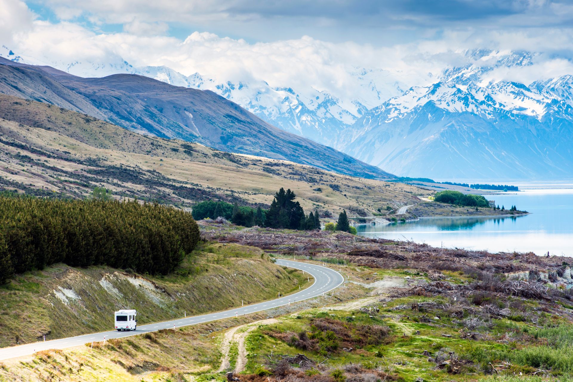 RV travelling along a scenic road near mountains and a lake in a remote landscape