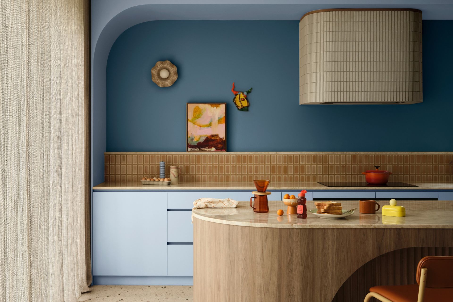 Playful kitchen with blue cabinetry, a curved wooden island, terracotta tiles and colourful accessories.