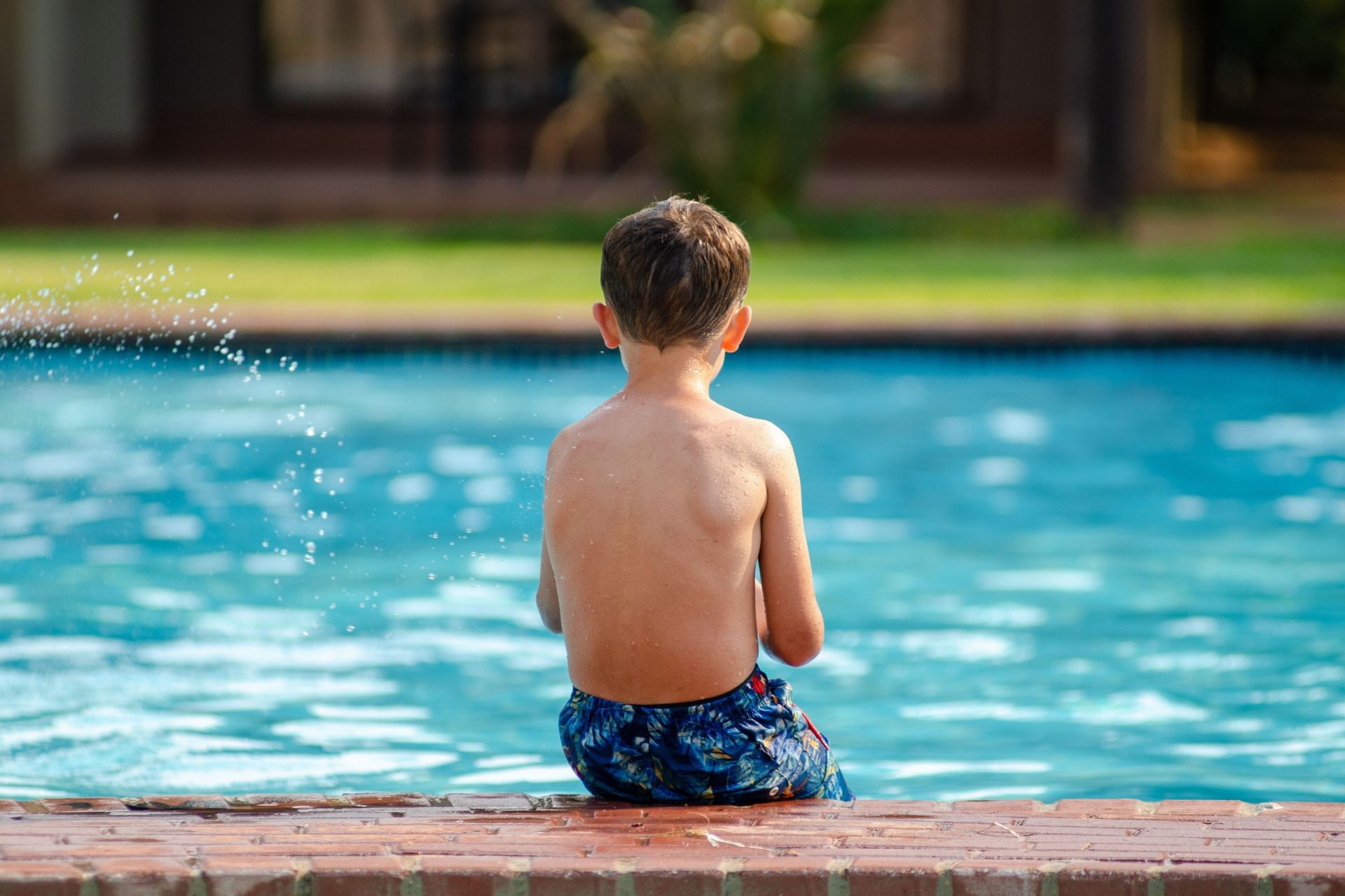 Young boy sitting at the edge of a backyard swimming pool.