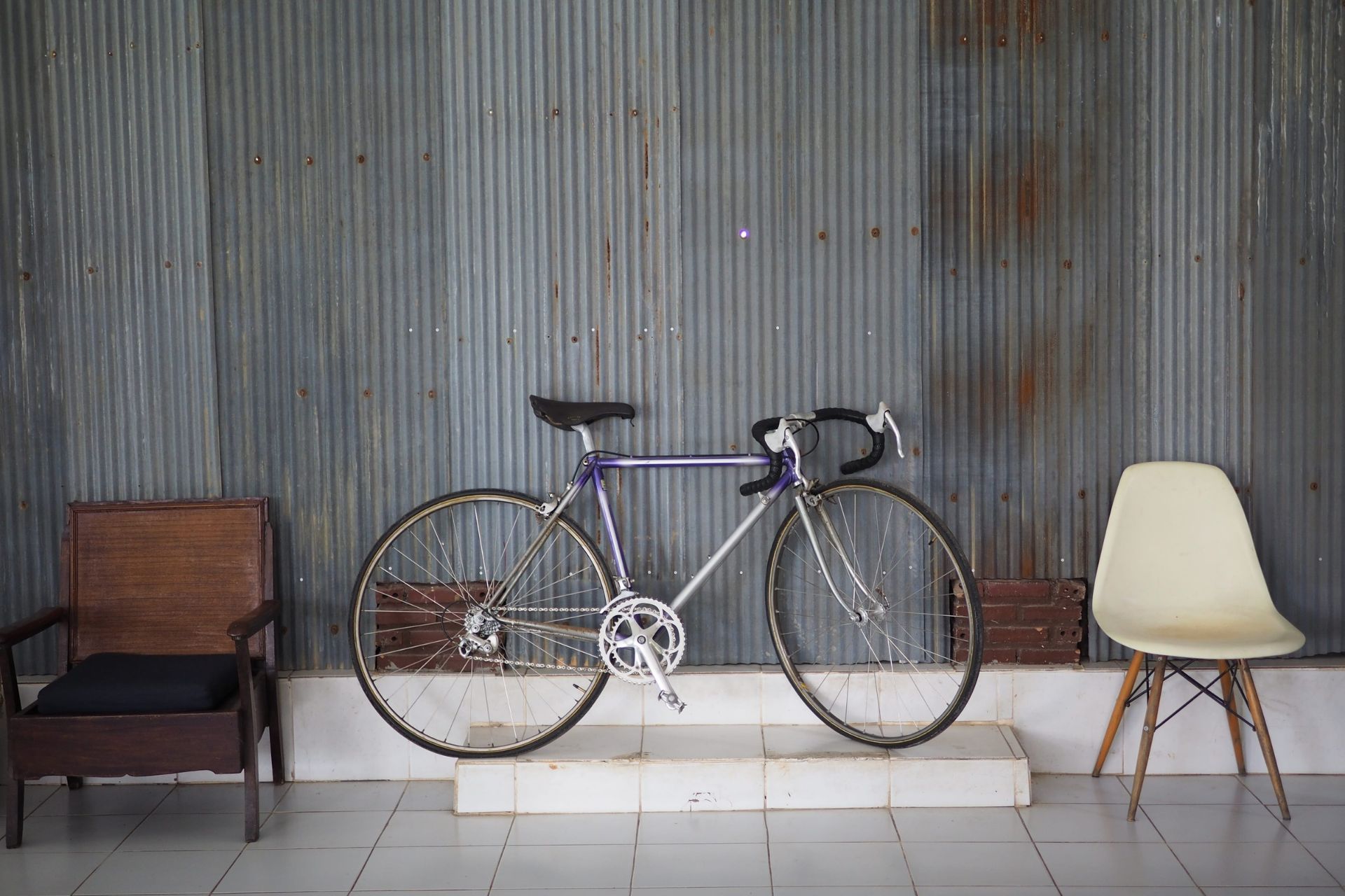 Vintage bicycle displayed between two chairs against a corrugated wall